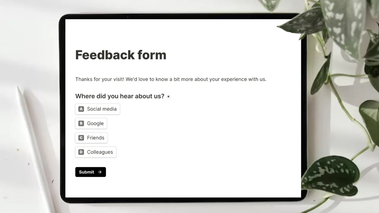 Photo of a tablet on a desk beside a stylus and a trailing pothos plant, showing a feedback form. It reads "Thanks for your visit! We'd love to know a bit more about your experience with us", then asks "Where did you hear about us?" with four options, social media, Google, friends and colleagues, above a Submit button.
